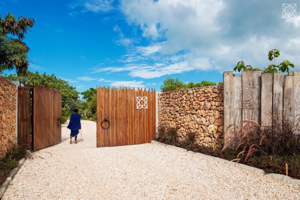 a woman walking through a gate with a stone wall at Zuri Zanzibar in Kendwa