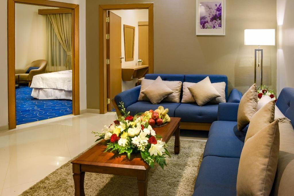 فيوري للشقق الفندقية في الأحساء: غرفة معيشة مع أريكة زرقاء وطاولة مع زهور