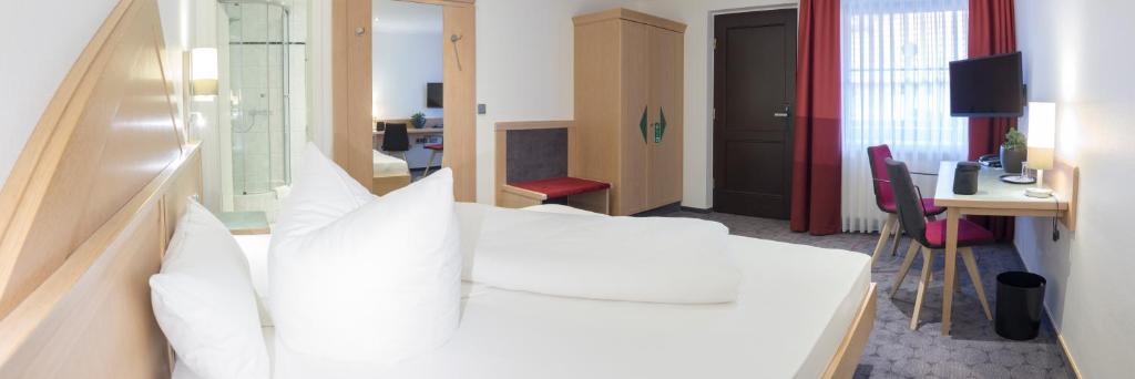 ElsterwerdaにあるHotel Weißes Roßの白いベッドとデスクが備わるホテルルームです。