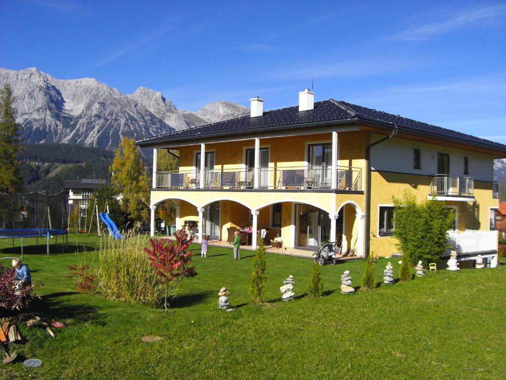 une grande maison jaune avec des montagnes en arrière-plan dans l'établissement Villa Castelli, à Schladming