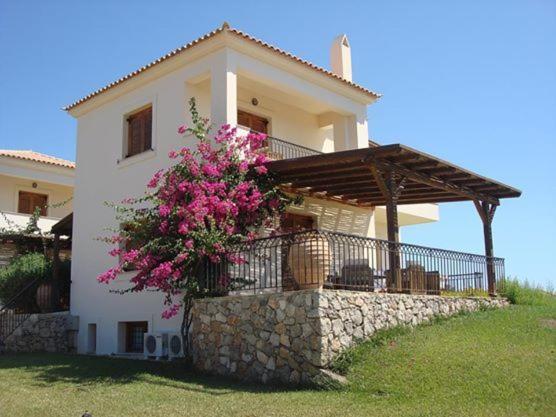 een wit huis met een hek en roze bloemen bij VILLA EVANTHIA in Bouzéïka