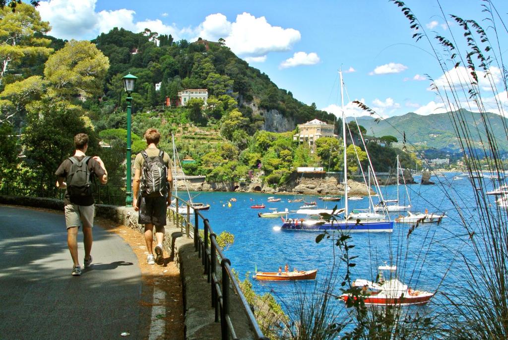 two people walking down a road near a river with boats at Albergo Annabella in Santa Margherita Ligure
