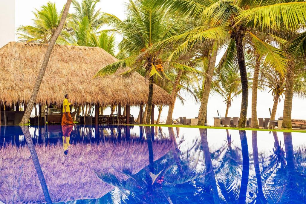 un homme debout à côté d'une piscine bordée de palmiers dans l'établissement Jetwing Sea, à Negombo