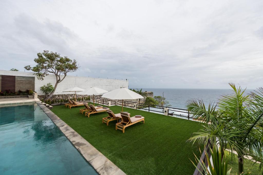 a pool with chairs and umbrellas next to the ocean at Villa Maiara in Uluwatu