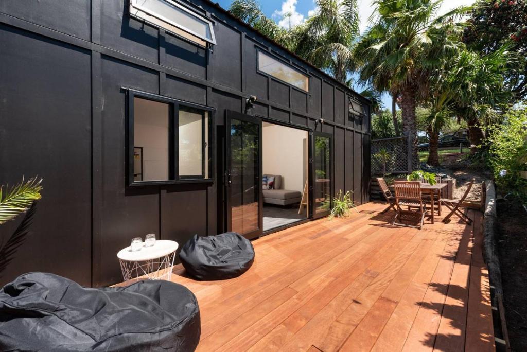 una pequeña casa negra con terraza de madera en Cozy Tiny House Hideaway, en Tauranga