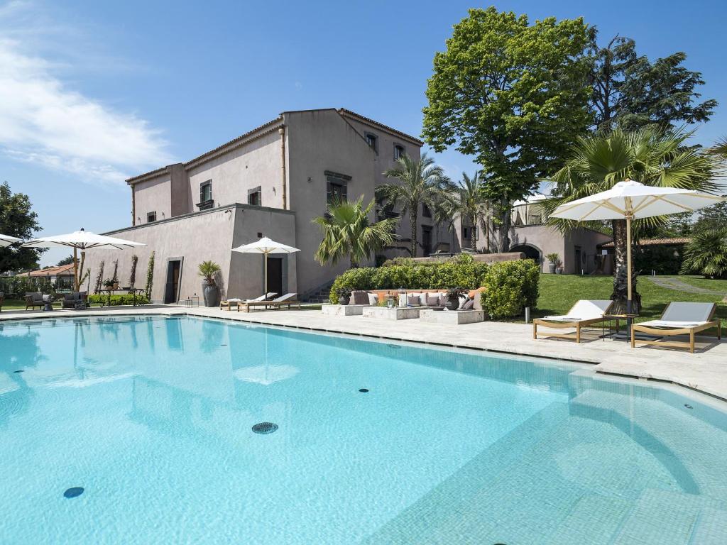 una piscina con sedie e ombrelloni di fronte a un edificio di Relais San Giuliano a Viagrande