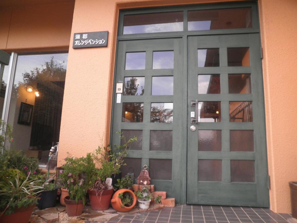 eine grüne Tür eines Gebäudes mit Topfpflanzen in der Unterkunft Orange Pension in Gamagori