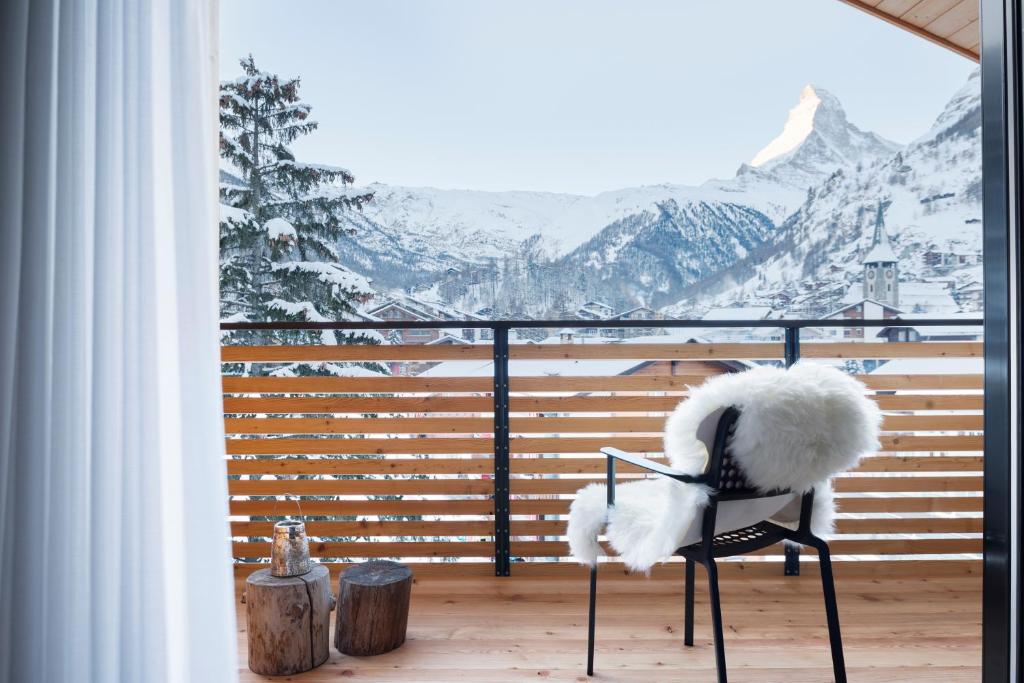 a chair on a balcony with a view of snow covered mountains at Haus-Ascot-Zermatt in Zermatt