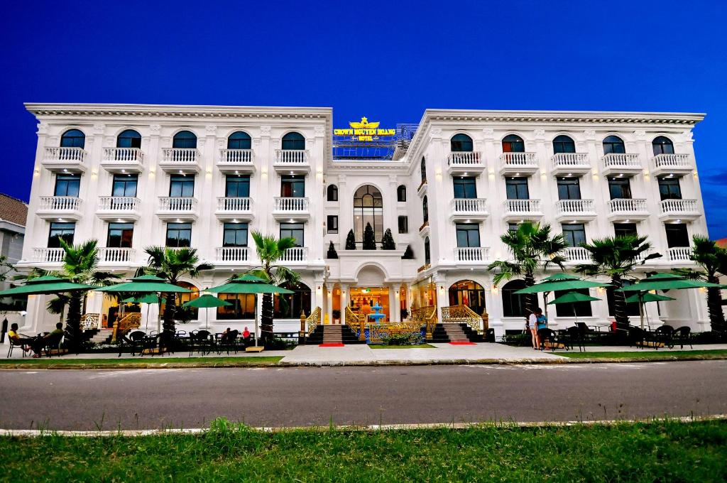 a large white building with green umbrellas in front of it at Crown Nguyen Hoang Hotel in Nha Trang