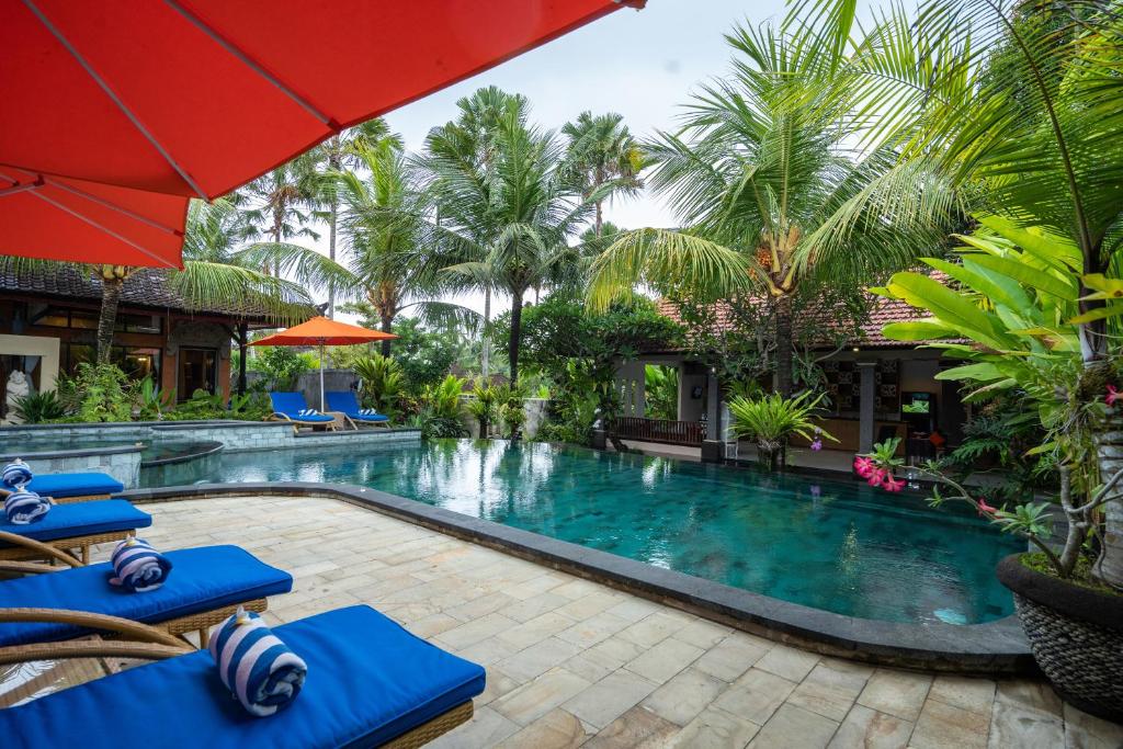 a patio area with a pool, chairs, and umbrellas at Natya Hotel Tanah Lot in Tanah Lot