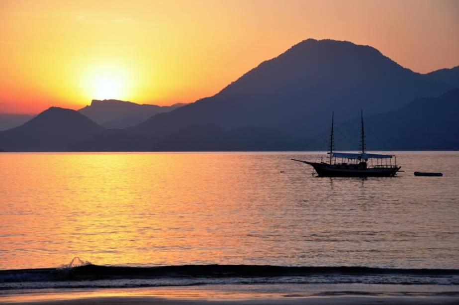 a boat in the water at sunset with a mountain at Apartamentos Petrópolis in Ubatuba