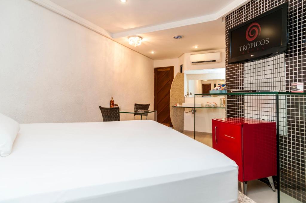Habitación de hotel con cama blanca y armario rojo en Trópicos Motel en Natal