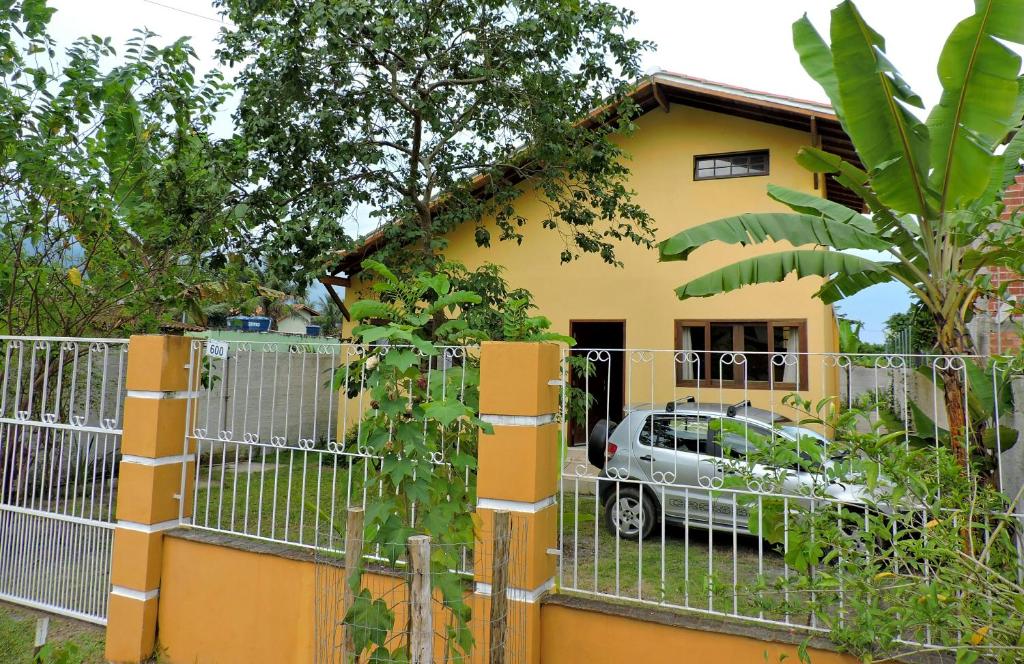 a fence in front of a yellow house with a car at Pouso Paratiense Jabaquara in Paraty