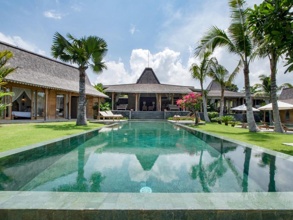 a swimming pool in front of a house with palm trees at Villa Mannao in Kerobokan