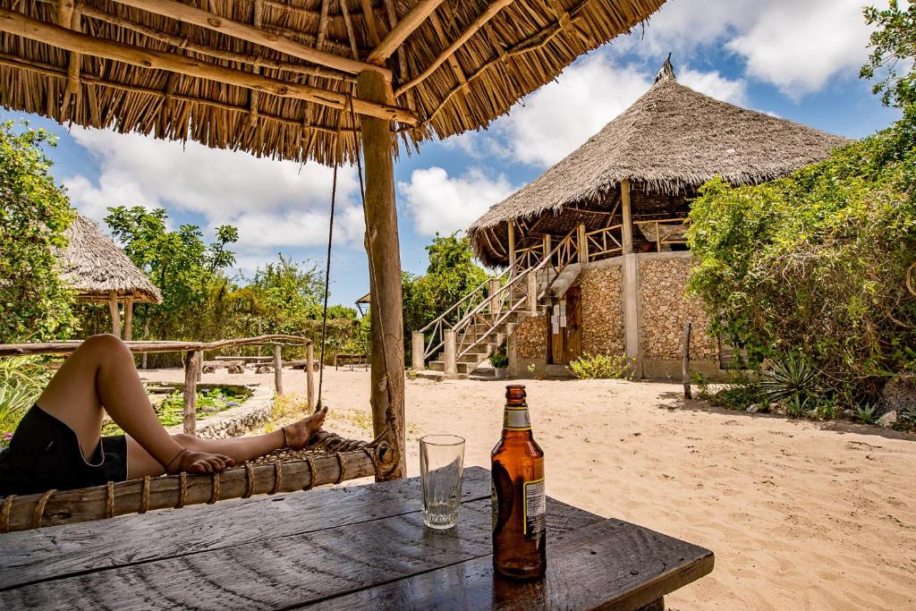 uma mulher sentada numa mesa com uma garrafa de cerveja em Mida Creek Eco Camp em Watamu