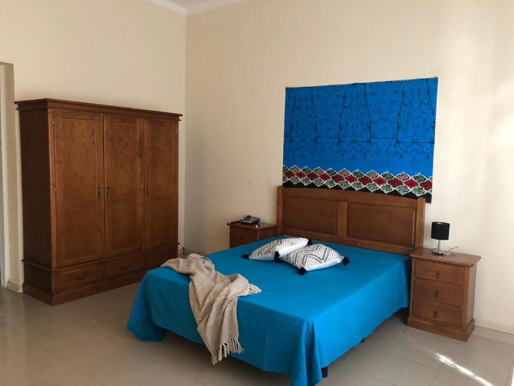 a bedroom with a blue bed and a wooden cabinet at Hospedaria Vianense in Luanda