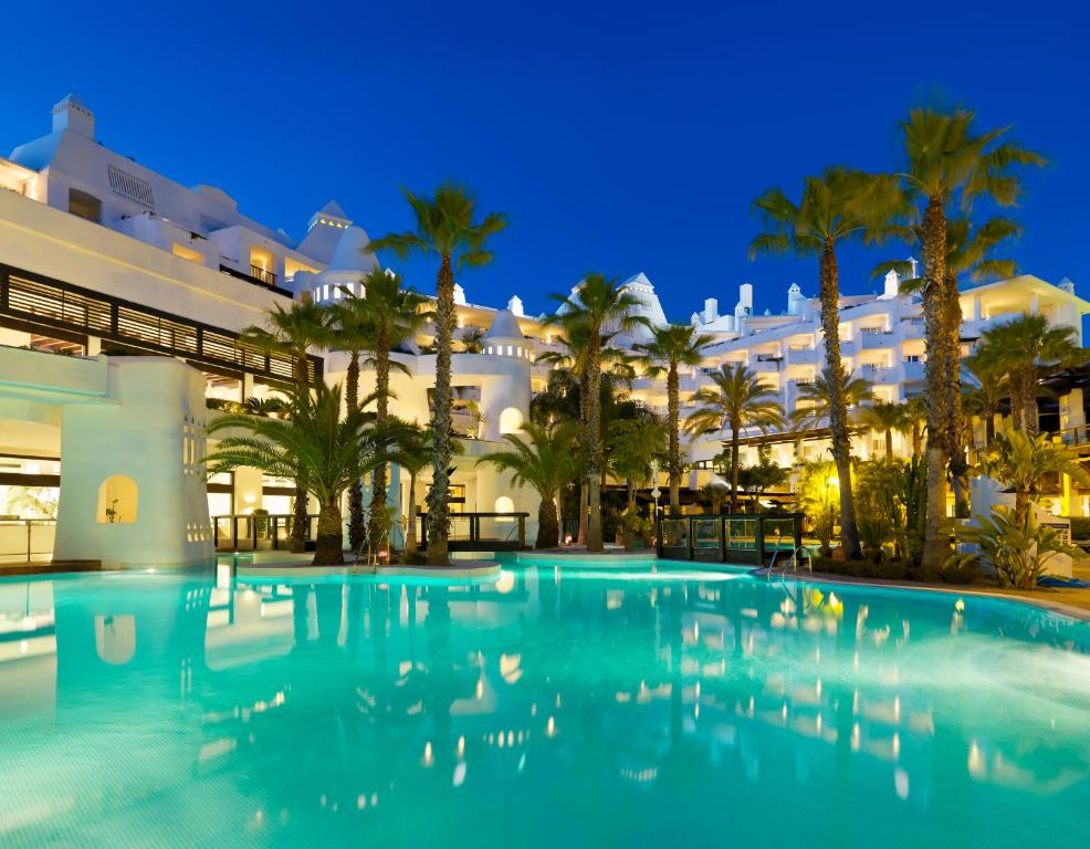 a large swimming pool in front of a building with palm trees at H10 Estepona Palace in Estepona