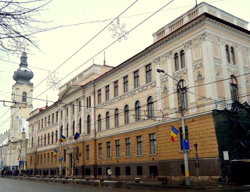 a large building with a clock tower on a street at Kollege Hostel in Cluj-Napoca