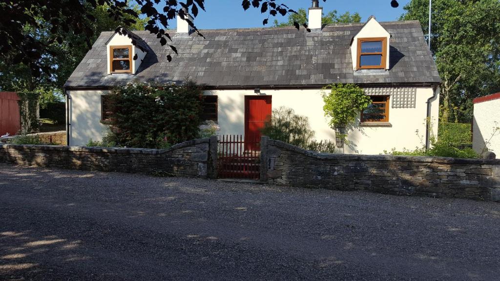 a white house with a red door and a stone wall at Millwood Cottage in Lisbellaw