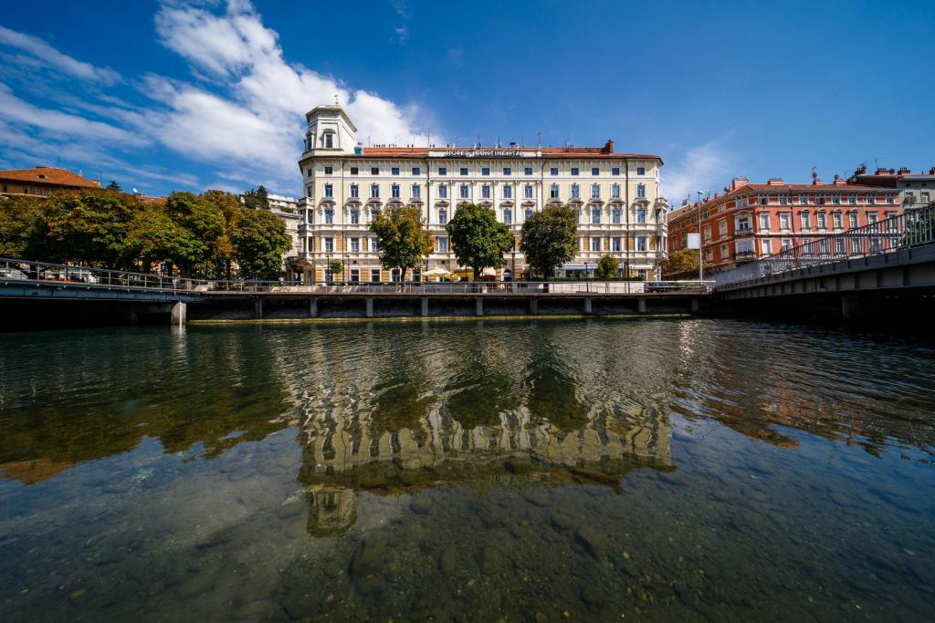 a building with a reflection in a body of water at Hotel Continental in Rijeka