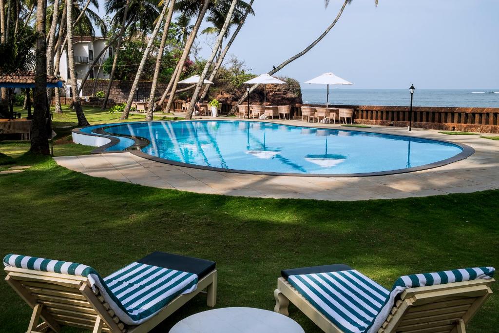 a swimming pool with two lounge chairs and the ocean at Prainha Resort By The Sea in Panaji
