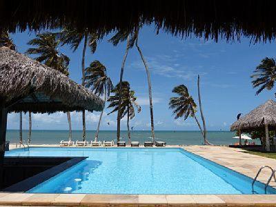 a swimming pool with chairs and umbrellas and the ocean at Eco Paradise Sunset Beach in Cumbuco