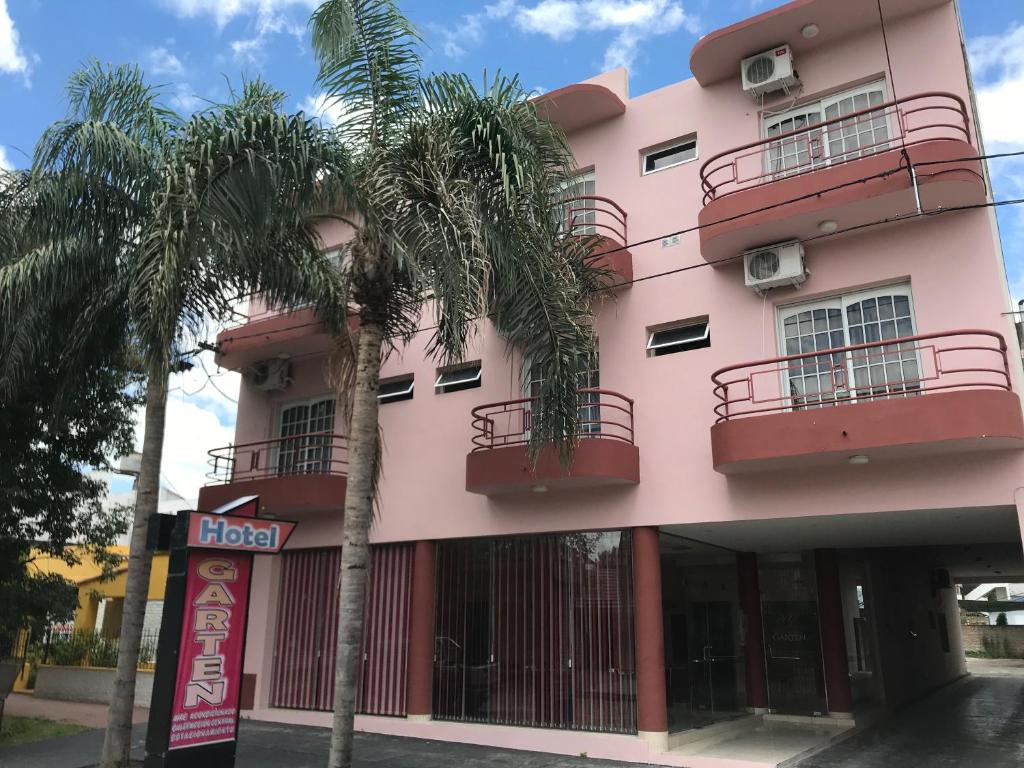 a pink building with palm trees in front of it at Hotelgarten in Crespo