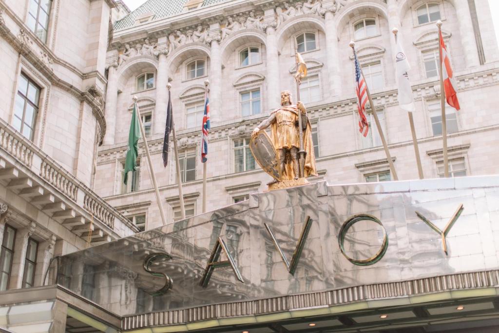 una statua di fronte a un edificio con bandiere di The Savoy a Londra