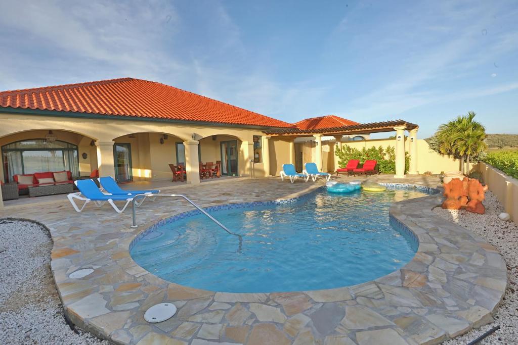 a home with a pool with blue chairs and a house at Aruba Dreams in Palm-Eagle Beach