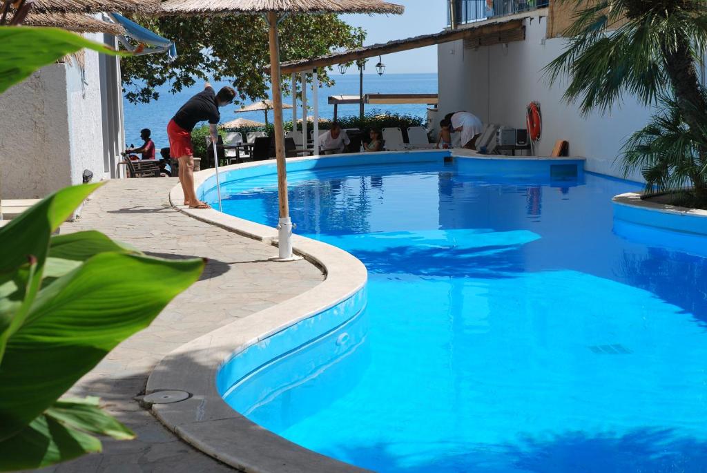 a man is standing next to a swimming pool at Hotel Kanelli Beach in Selianitika