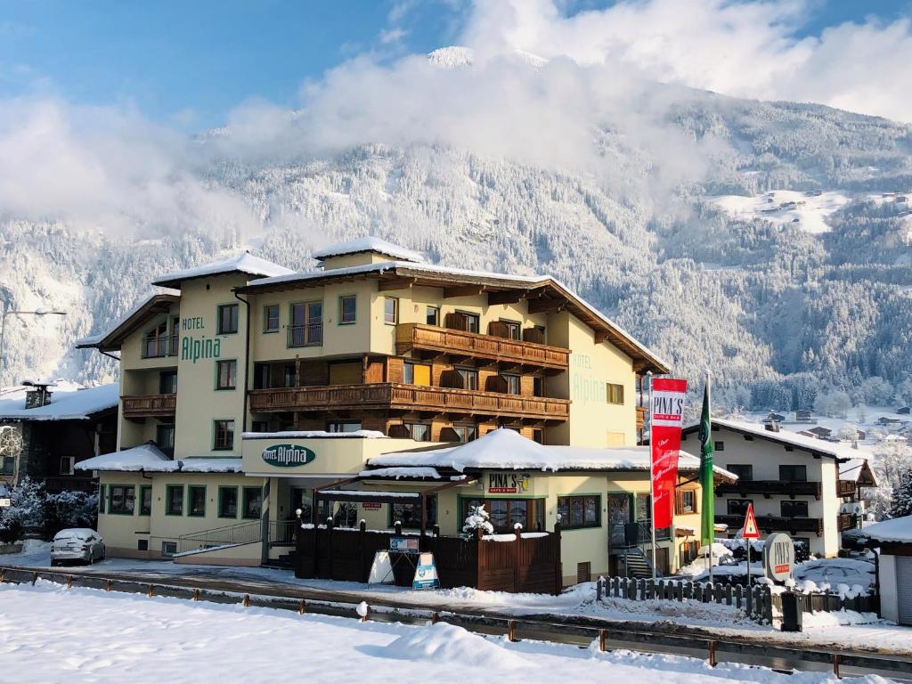 een groot gebouw met een met sneeuw bedekte berg op de achtergrond bij Hotel Alpina in Ried im Zillertal