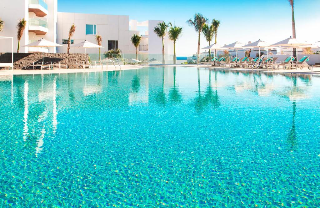 a large swimming pool with blue water and palm trees at Hotel Lava Beach in Puerto del Carmen