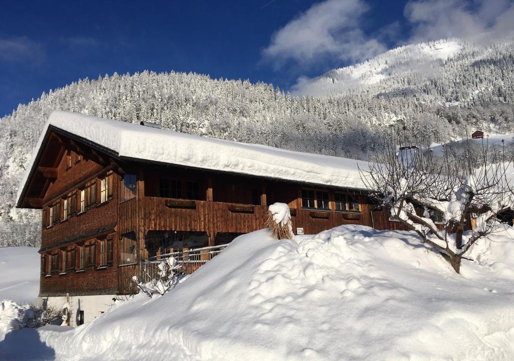Cabaña de madera cubierta de nieve con una pila de nieve en Rüf Stefanie, en Au im Bregenzerwald