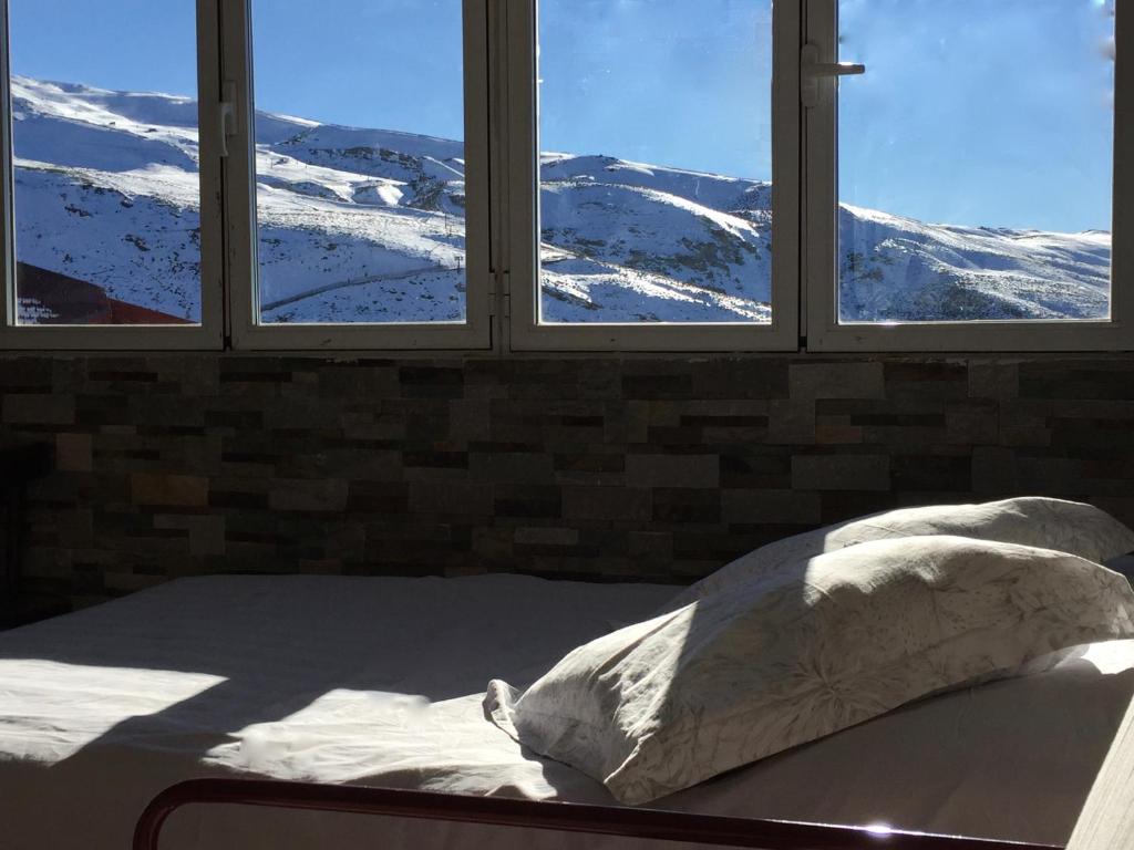 a bed in a room with three windows with snow covered mountains at Sol del Sur Sierra Nevada in Sierra Nevada