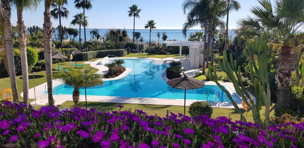 una piscina con palmeras y flores púrpuras en Costalita Seaview, en Estepona