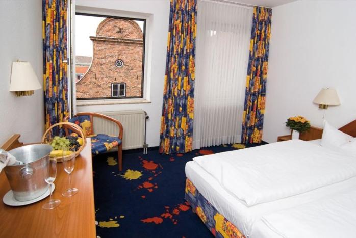 Hotel Alter Speicher في لوبيك: غرفه فندقيه بسرير ومكتب ونافذه