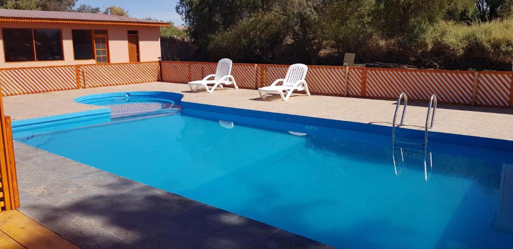 una piscina con 2 sillas blancas al lado en Ckausama North, en San Pedro de Atacama