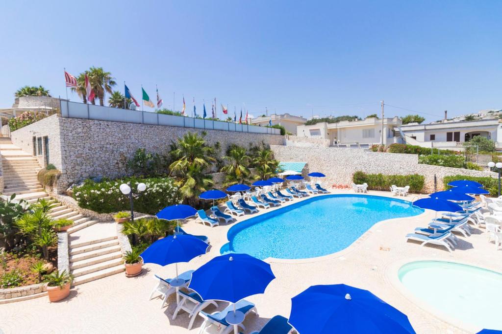an outdoor swimming pool with blue umbrellas and chairs at Hotel Ristorante Panoramico in Castro di Lecce