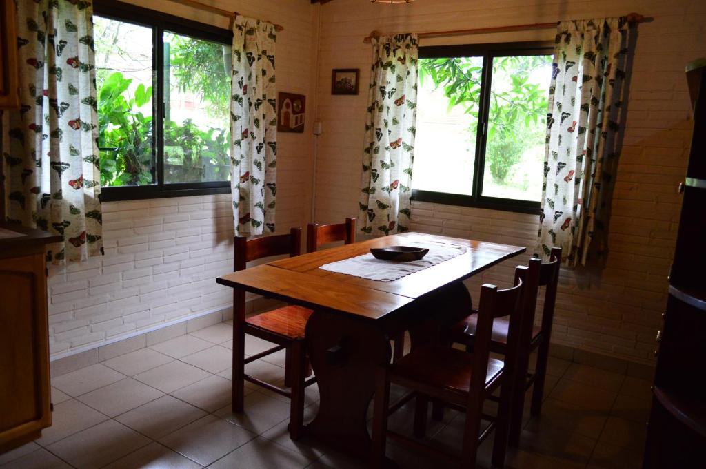 a dining room with a wooden table and some windows at Oasis Bed and Breakfast in Puerto Iguazú