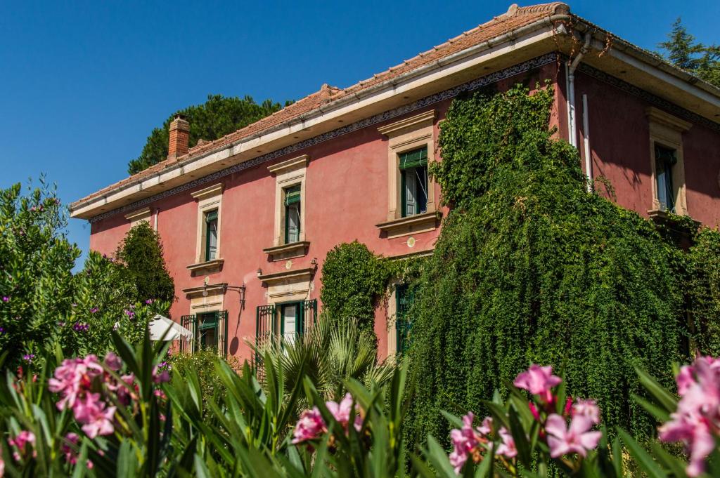 un edificio cubierto de hiedra con flores rosas delante de él en Affascinante Villa Ottocentesca a Caltagirone en Caltagirone