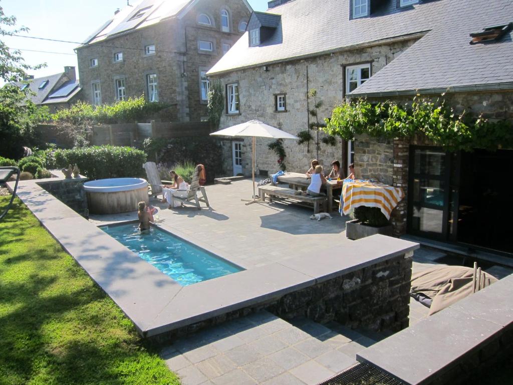 einen Hinterhof mit einem Pool und Menschen sitzen um einen Tisch in der Unterkunft Maison de charme à Crupet et le gîte la suite in Crupet