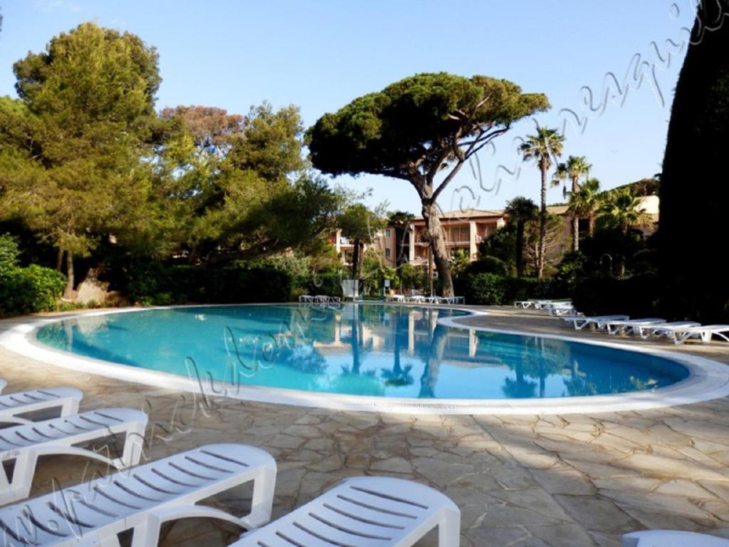 una gran piscina con sillas blancas y árboles en Magnifique Parc de la Presqu'île avec Piscine et Plage face à Porquerolles !, en Hyères