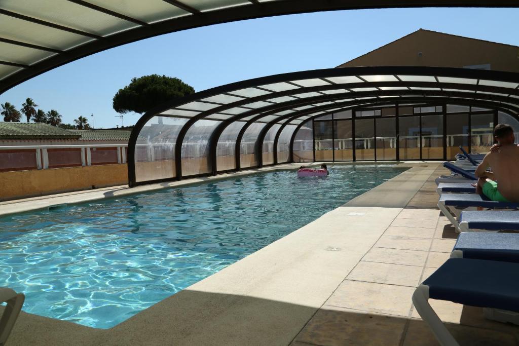 a swimming pool with a retractable roof and blue chairs at Hotel Myriam Vias Plage in Vias