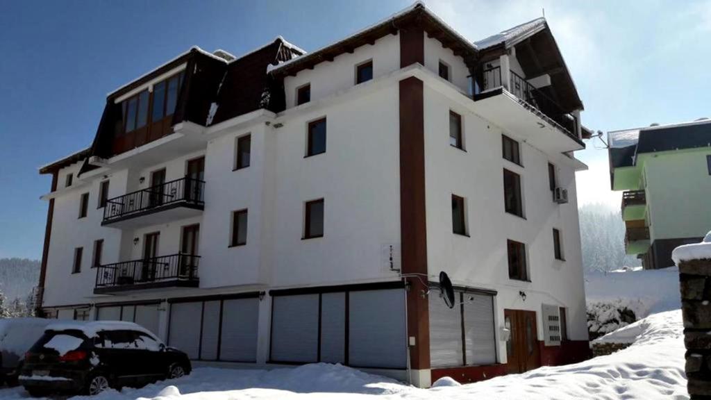 Apartments Vlašić في فلاسيتش: مبنى أبيض كبير مع سيارة متوقفة في الثلج