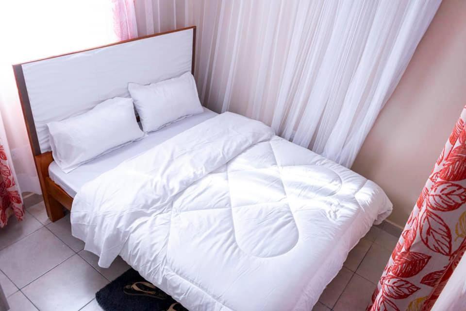 Serene Homes في مومباسا: سرير بشرشف ووسائد بيضاء في الغرفة