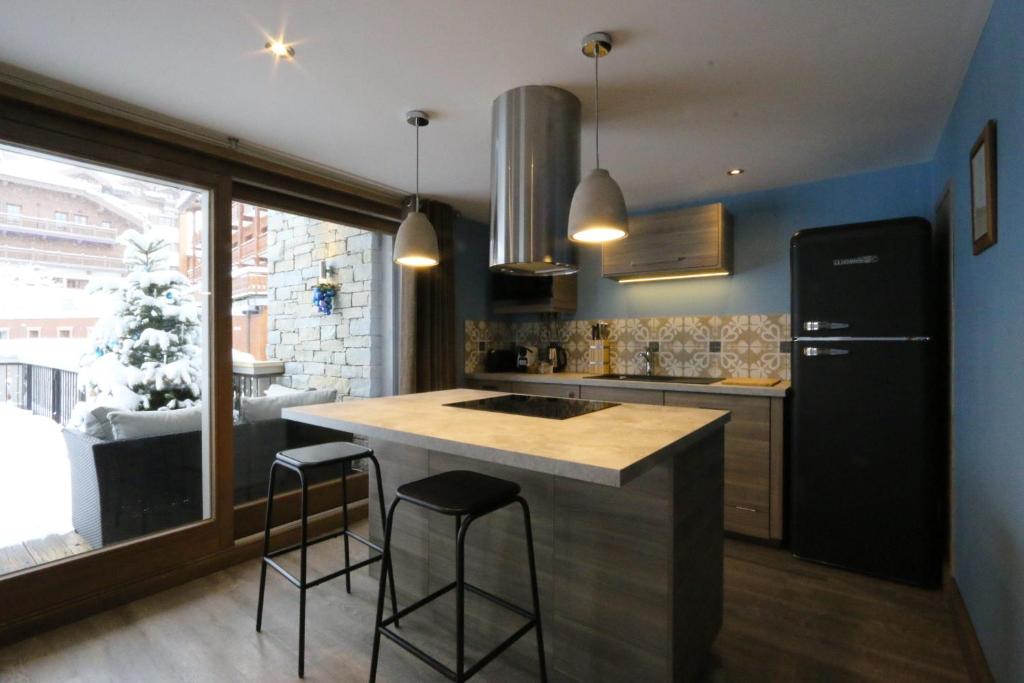 a kitchen with a black refrigerator and two bar stools at Hotel Edelweiss in Courchevel