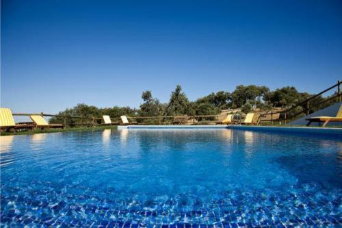 una gran piscina con agua azul y sillas en Hotel Quinta Dos Bastos, en Évora