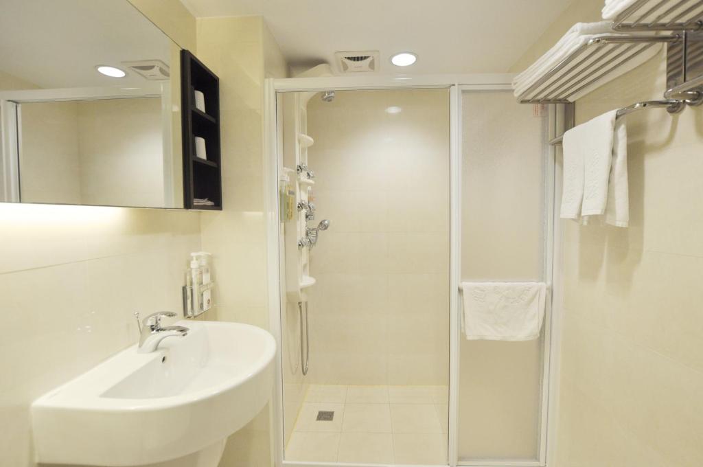 a white bathroom with a sink and a shower at Kindness Hotel-Qixian in Kaohsiung