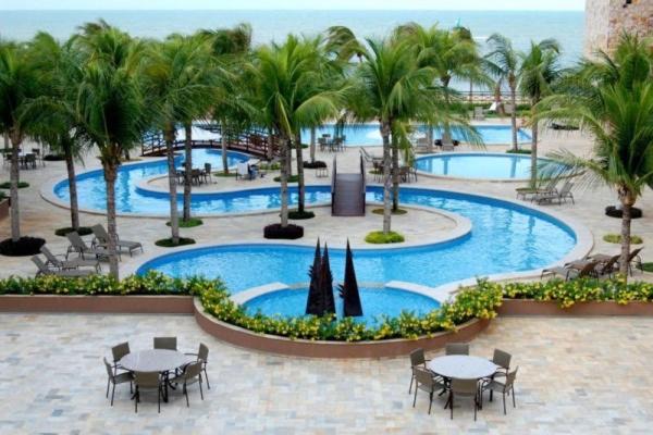 een zwembad van het resort met tafels en stoelen en palmbomen bij Kariri Apartaments Sunset Beach in Cumbuco
