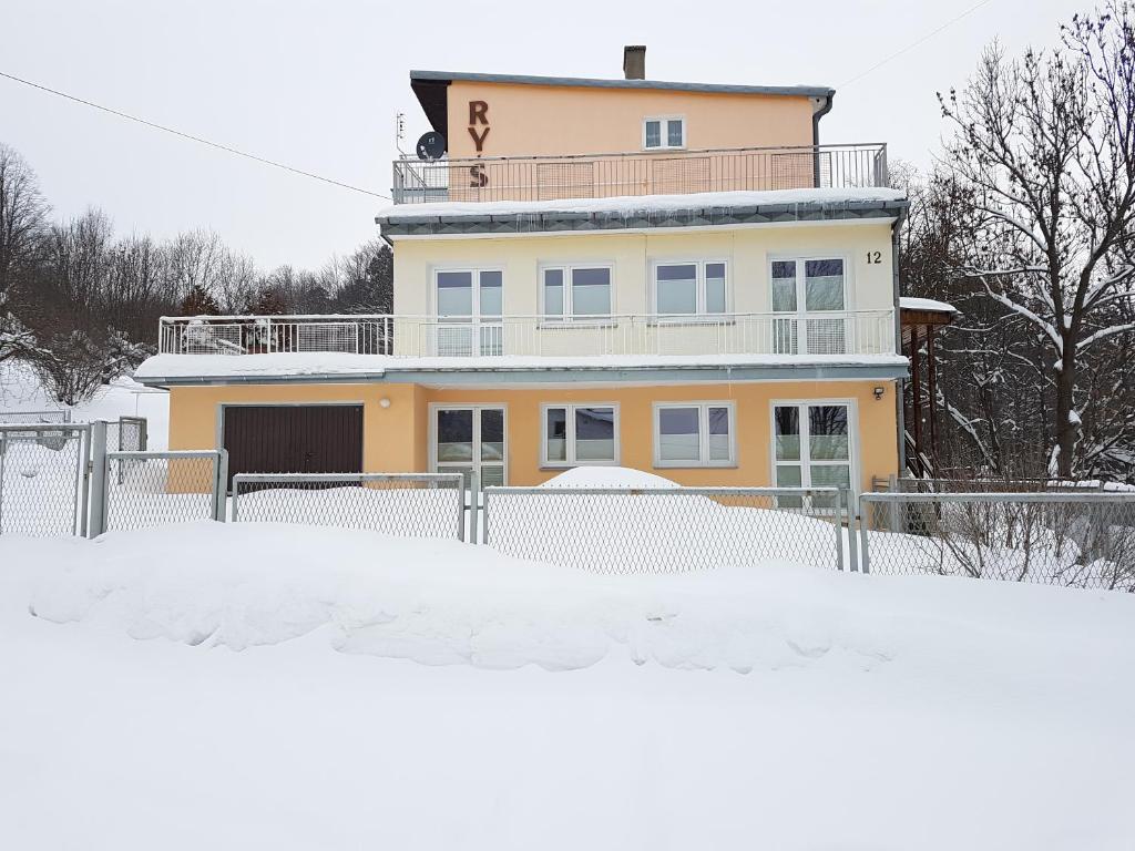 a large yellow house with a fence in the snow at Willa RYŚ in Krynica Zdrój